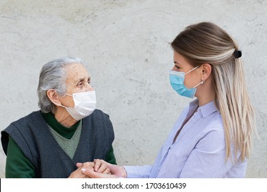 Portrait of friendly caregiver posing with elderly ill woman wearing surgical mask because of covid-19 pandemic