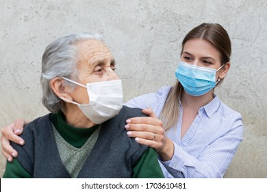 Portrait Of Friendly Caregiver Posing With Elderly Ill Woman Wearing Surgical Mask Because Of Covid-19 Pandemic