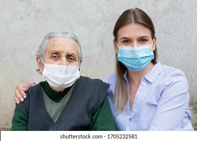 Porträt einer freundlichen Betreuerin, die sich mit einer älteren kranken Frau ausstellt, die wegen einer Covid-19-Pandemie eine chirurgische Maske trägt