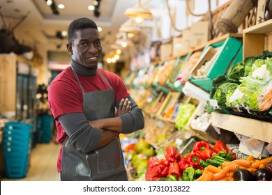 Portrait of friendly confident African American salesman of fruit and vegetable store standing near counter