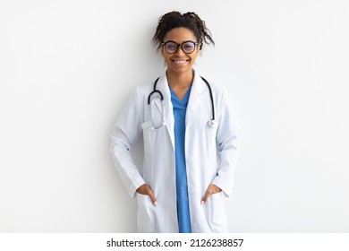 Portrait Of Friendly Female Black Doctor In Glasses Looking At Camera Standing And Posing Isolated Over White Studio Background Wall, Lady Wearing Blue Uniform, Coat And Stethoscope, Banner