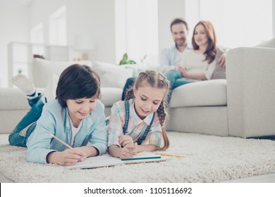 Portrait friendly lovely brother   sister drawing in album together lying carpet stomach using pen colorful pencils  mom   dad blurred background enjoying time together