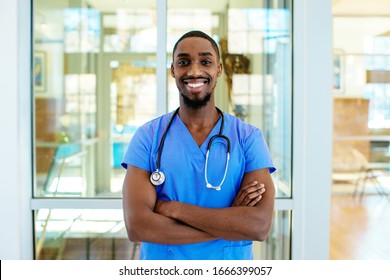 Portrait of a friendly male doctor or nurse wearing blue scrubs uniform and stethoscope, with arms crossed in hospital