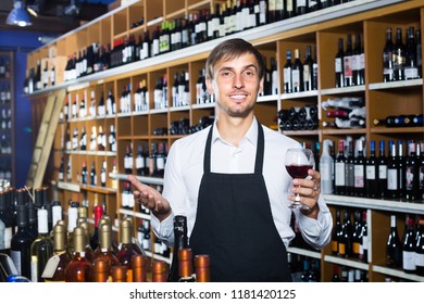 Portrait Of Friendly Male Seller In Uniform Promoting To Taste Wine Before Purchasing It In Wine Store
