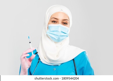 Portrait of a friendly Muslim doctor or nurse in hijab and medical face mask holding a syringe on a gray background. the concept of vaccination of the population or injection plastic of the face - Powered by Shutterstock