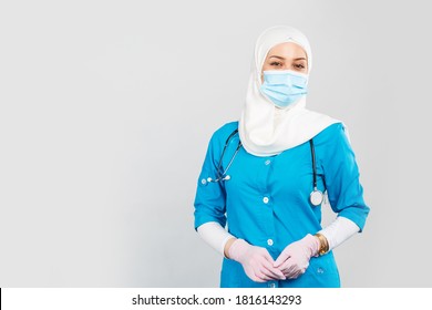 Portrait of a friendly Muslim doctor or nurse wearing hijab and medical face mask and gloves on a gray background.