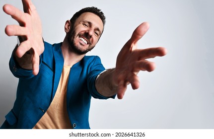 Portrait of friendly smiling adult man in casual blue jacket and yellow t-shirt holding out his hands fingers spread out, going to hug or take something over white background with copy space. Banner