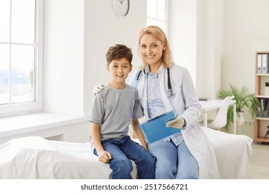 Portrait of a friendly smiling female doctor pediatrician holding report file with appointment and hugging a child boy patient during medical examination in clinic sitting on couch. - Powered by Shutterstock