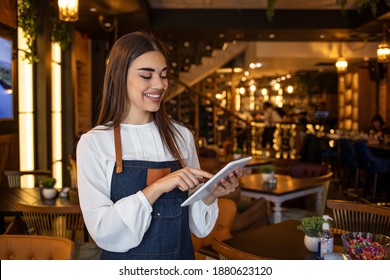 Portrait of friendly waitress holding a tablet computer looking at the camera smiling. Portrait of a smiling coffee shop owner standing inside her shop and using digital tablet - Powered by Shutterstock