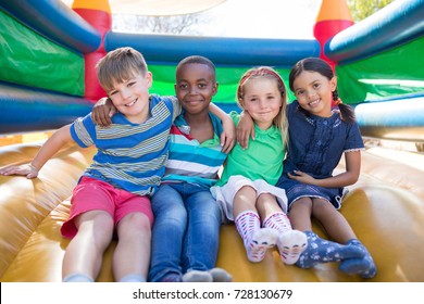 Portrait of friends with arms around sitting on bouncy castle at playground - Shutterstock ID 728130679