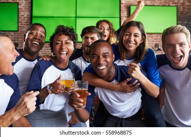 Portrait Of Friends Watching Game In Sports Bar On Screens