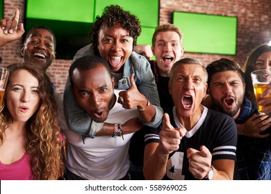 Portrait Of Friends Watching Game In Sports Bar On Screens