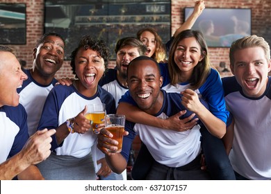 Portrait Of Friends Watching Game In Sports Bar On Screens