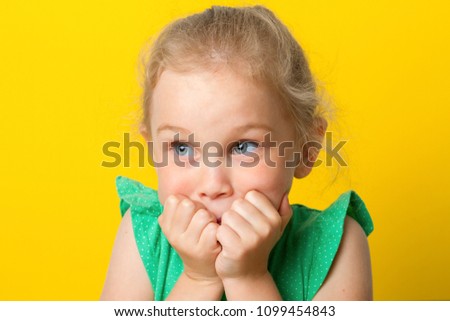 Portrait of a frightened girl holding hands at her face over yellow background