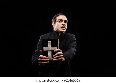 Portrait of frightened young catholic priest against black background - Shutterstock ID 623466065