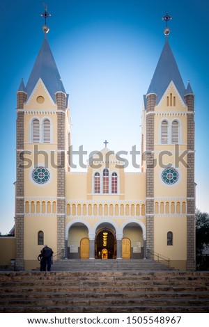 Portrait Front View - Saint Mary's Peach Coloured/Colored Twin Tower Cathedral With Open Door, Against A Clear Blue Namibian Sky, With Brown Stairs - Roman Catholic Church City Center Windhoek Namibia