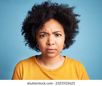 Portrait, frown and anger with an african woman on a blue background in studio looking mad or serious. Face, bad or negative and an unhappy young female person with an afro feeling frustrated