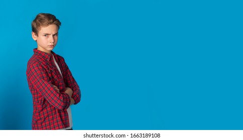 Portrait Of Frowning Grumpy Teen Boy Standing With Folded Arms Over Blue Background, Panorama With Copy Space