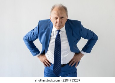 Portrait of frowning mature businessman looking at camera. Senior manager wearing formalwear standing with hands on hips against white background. Angry boss concept - Shutterstock ID 2204733289