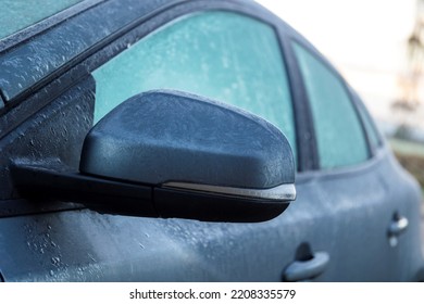 A portrait of a frozen side mirror of a completely frozen car during winter time. The ice first needs to melt or be removed before the driver can safely start the journey.
