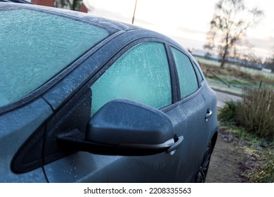 A portrait of a frozen side mirror and side windows of a completely frozen car during winter time. The ice first needs to melt or be removed before the driver can safely start the journey.