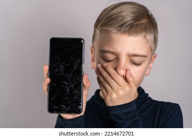 Portrait Frustrated Kid With Broken Mobile Phone Screen, Shocked With Shame For Mistake, Expression Of Fear. Scared Teen Boy With Emotional Expression Showing Broken Smartphone.