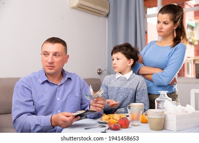 Portrait Of Frustrated Man Giving Money To Strict Wife And Tween Boy In Home Interior