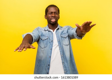 Portrait of frustrated man with poor sight wearing denim casual shirt standing with closed eyes and stretching hands, searching way, blindness concept. indoor studio shot isolated on yellow background