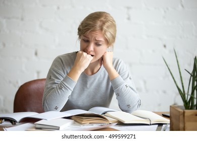 Portrait of a frustrated student girl sitting at the desk biting her fist. Education concept photo, lifestyle
