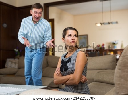 Portrait of frustrated woman sitting on sofa in living room on background with angry screaming husband
