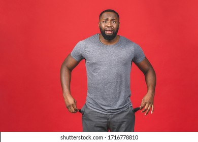 Portrait Of Frustrated Worried African American Black Man With Beard In Casual Turning Out Empty Pockets Showing I Have No Money Gesture, Bankrupt. Isolated On Red Background.