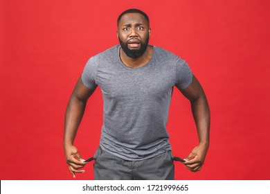 Portrait of frustrated worried african american black man with beard in casual turning out empty pockets showing I have no money gesture, bankrupt. Isolated on red background.