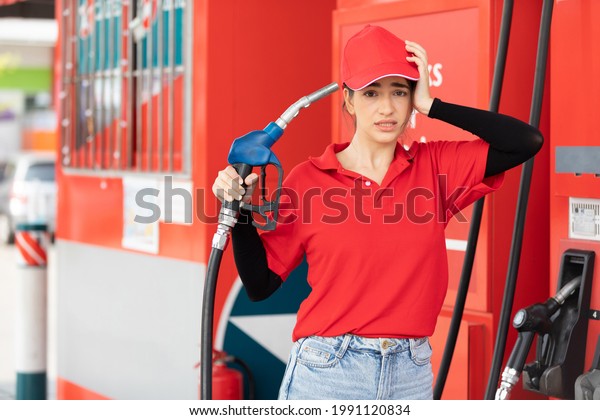 portrait frustrated\
young woman worker holding petrol hose and her face a trouble\
something at the gas\
station