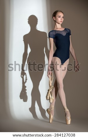 Portrait in full growth graceful ballerina in a studio on a white background. Dancer in a blue bathing suit. Against the background of her beautiful shadow.