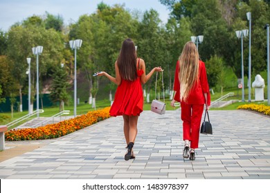 Portrait in full growth, two stylish beautiful girlfriends in red clothes walk along the promenade