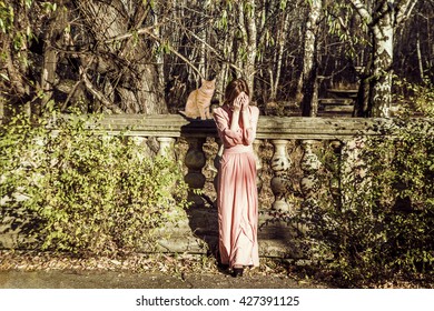 Portrait Full Length Of Beautiful Young Adult Slim Caucasian Woman Stand Against Abandoned Old Fence. Redhead Cute Girl Wear Long Fashion Dress. Hands On Face And Close The Eyes