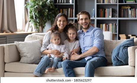 Portrait of full relaxed family with adorable little children, sitting on sofa. Happy young couple parents embracing small kids daughters, enjoying free leisure weekend time together in living room. - Shutterstock ID 1805623297