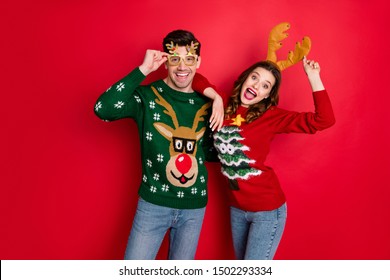 Portrait Of Funky Crazy Two People  Wife Husband In Brown Antlers Costume Lean Shoulder Wear Denim Seasonal Clothes Christmas Tree Design Pullover Jumper Spectacles Isolated Over Red Color Background