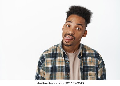 Portrait Of Funny African American Man Showing Silly Faces, Tongue And Grimace At Camera, Having Fun, Standing In Casual Checked Shirt Over White Background