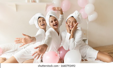 Portrait funny Asian bride with bridesmaids sitting on bed in soa or hotel, having fun at hen party, three happy beautiful young women wearing white bathrobes and towels on head looking at camera - Powered by Shutterstock