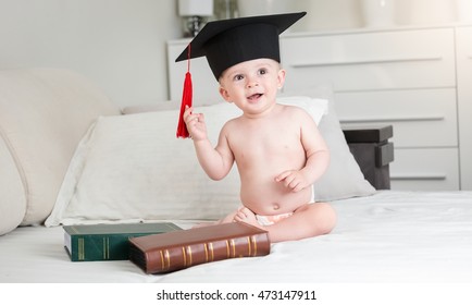 Portrait of funny baby boy in diapers wearing black graduation cap 