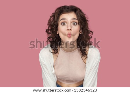 Portrait of funny beautiful brunette young woman with curly hairstyle in casual style standing with big eyes and fish lips looking at camera. indoor studio shot isolated on pink background.