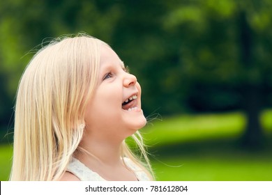 Portrait Of Funny Blond Little Caucasian Girl Looking Up And Smiling Outdoors