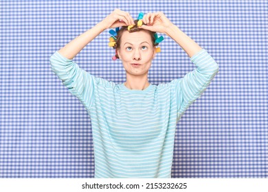 Portrait Of Funny Blond Young Woman Putting Her Hair Into Bright Colorful Curlers, Looking Very Busy, Standing Over Shower Curtain Background In Bathroom. Beauty And Morning Routine Concept