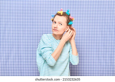 Portrait Of Funny Blond Young Woman Putting Her Hair Into Bright Colorful Curlers, Looking Busy, Frowning Face, Standing Over Shower Curtain Background In Bathroom. Beauty And Morning Routine Concept