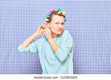 Portrait Of Funny Blond Young Woman Putting Her Hair Into Bright Colorful Curlers, Looking Busy, Frowning Face, Standing Over Shower Curtain Background In Bathroom. Beauty And Morning Routine Concept