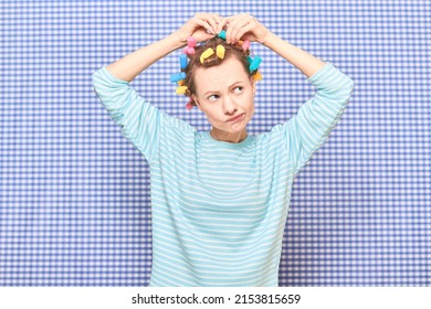 Portrait Of Funny Blond Young Woman Putting Her Hair Into Bright Colorful Curlers, Looking Busy, Frowning Face, Standing Over Shower Curtain Background In Bathroom. Beauty And Morning Routine Concept