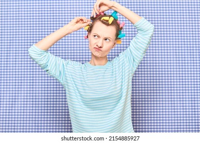 Portrait Of Funny Blond Young Woman Putting Her Hair Into Bright Colorful Curlers, Looking Busy, Frowning Face, Standing Over Shower Curtain Background In Bathroom. Beauty And Morning Routine Concept