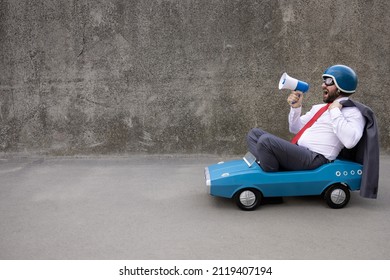 Portrait of funny businessman outdoor. Man driving retro pedal car and shouting through loudspeaker. Back to work, start up and business idea concept