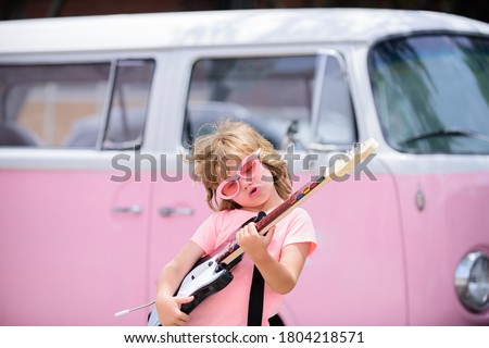 Portrait of a funny child with pink glasses practicing a song during a guitar lesson on street. Music concept, kids music school. Rock concert